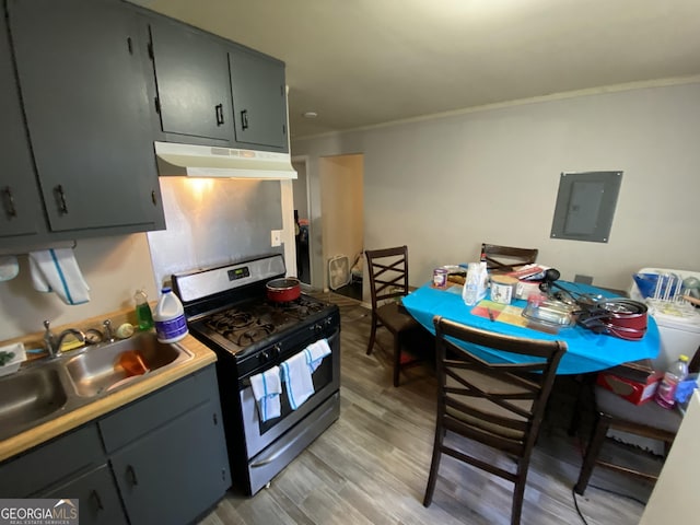 kitchen with stainless steel gas range oven, under cabinet range hood, electric panel, a sink, and light wood finished floors