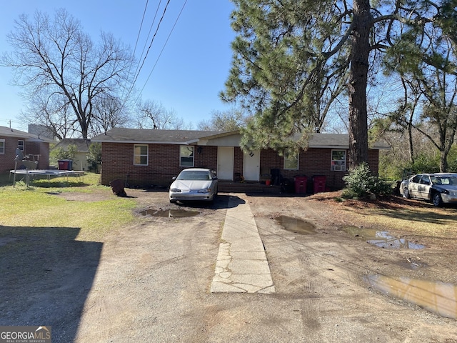 single story home with brick siding, driveway, a front lawn, and a trampoline