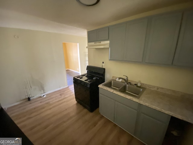 kitchen with light wood-style flooring, gray cabinets, under cabinet range hood, a sink, and black range with gas cooktop