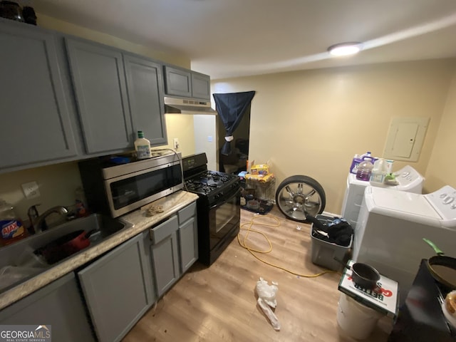 kitchen featuring gray cabinetry, washer and dryer, stainless steel microwave, under cabinet range hood, and black gas range oven