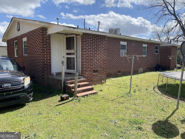 back of house featuring brick siding, a yard, and a trampoline