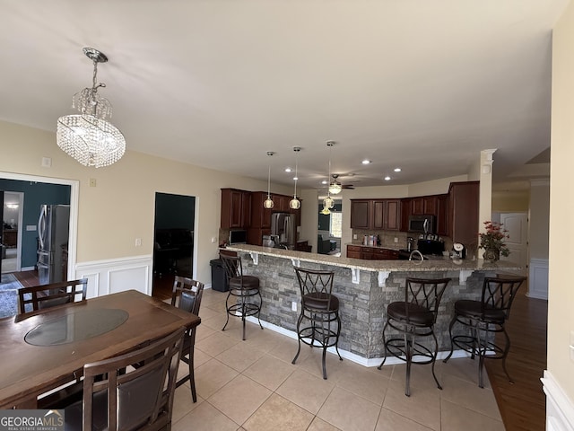 kitchen featuring ceiling fan with notable chandelier, stainless steel appliances, a peninsula, and a kitchen bar