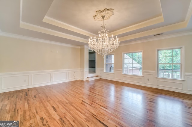 unfurnished dining area with a chandelier, a raised ceiling, light wood-style flooring, and visible vents