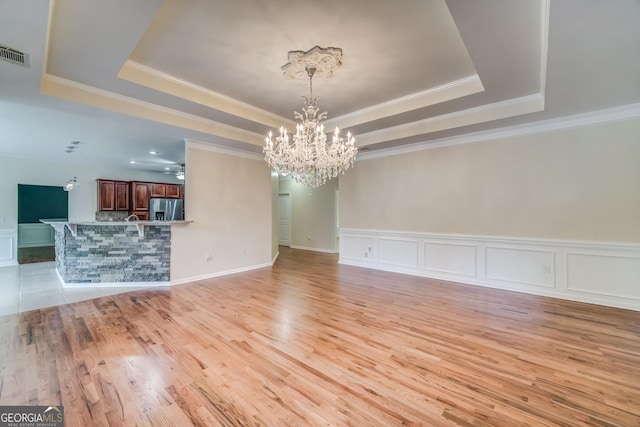 unfurnished dining area with a chandelier, a raised ceiling, and ornamental molding