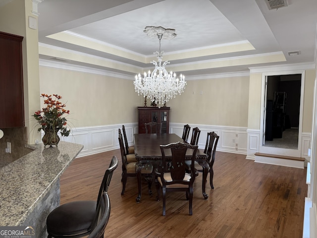 dining area featuring crown molding, a decorative wall, a raised ceiling, and dark wood finished floors