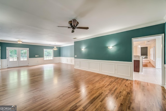 spare room with a decorative wall, crown molding, wainscoting, light wood-style floors, and ceiling fan