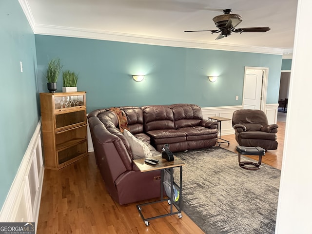 living room featuring ceiling fan, crown molding, a wainscoted wall, and wood finished floors