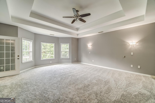 spare room with a tray ceiling, carpet, a ceiling fan, and baseboards