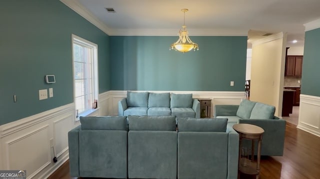 living room featuring visible vents, crown molding, dark wood-type flooring, wainscoting, and a decorative wall