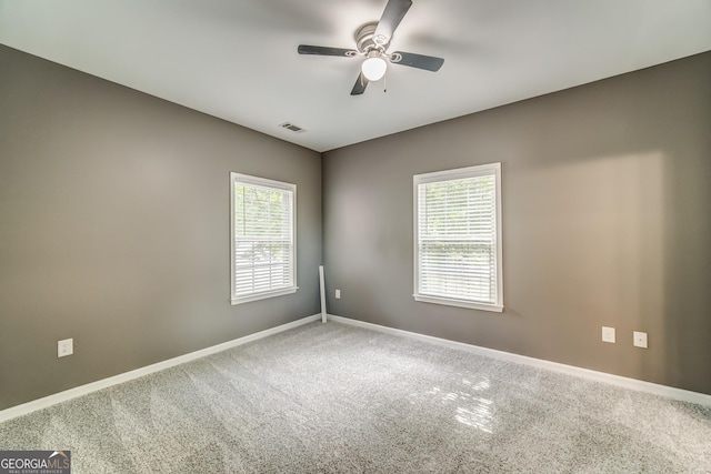 carpeted empty room with baseboards, visible vents, a ceiling fan, and a wealth of natural light