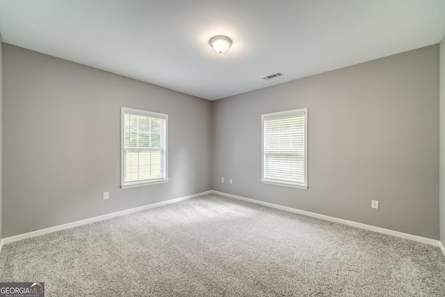 unfurnished room featuring carpet floors, visible vents, baseboards, and a wealth of natural light