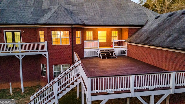 rear view of property featuring a shingled roof, brick siding, and stairs
