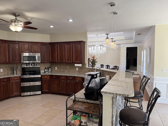 kitchen featuring a peninsula, light tile patterned flooring, ceiling fan with notable chandelier, crown molding, and appliances with stainless steel finishes