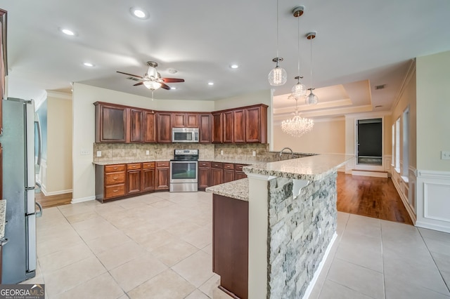 kitchen featuring a peninsula, light tile patterned flooring, ceiling fan with notable chandelier, light stone countertops, and appliances with stainless steel finishes