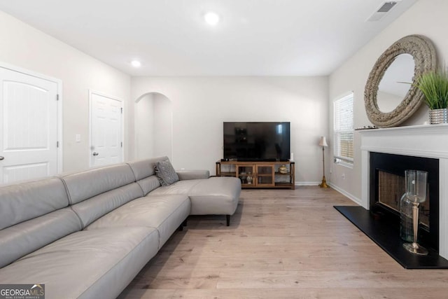 living area featuring visible vents, light wood-style flooring, recessed lighting, a fireplace with raised hearth, and arched walkways