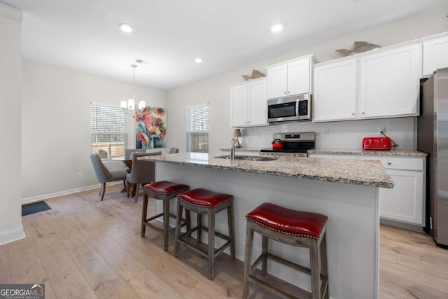 kitchen with a sink, light wood-style floors, tasteful backsplash, and appliances with stainless steel finishes