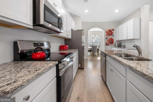 kitchen featuring a sink, arched walkways, appliances with stainless steel finishes, white cabinets, and light wood finished floors