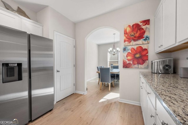 kitchen featuring baseboards, light stone countertops, light wood-style flooring, stainless steel refrigerator with ice dispenser, and white cabinetry