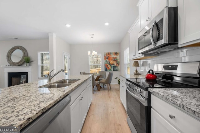 kitchen with a sink, white cabinets, appliances with stainless steel finishes, and a notable chandelier