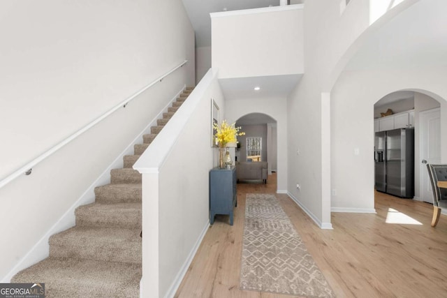 foyer with baseboards, arched walkways, a high ceiling, light wood-type flooring, and stairway