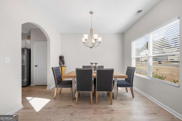 dining area featuring baseboards, arched walkways, an inviting chandelier, and light wood finished floors