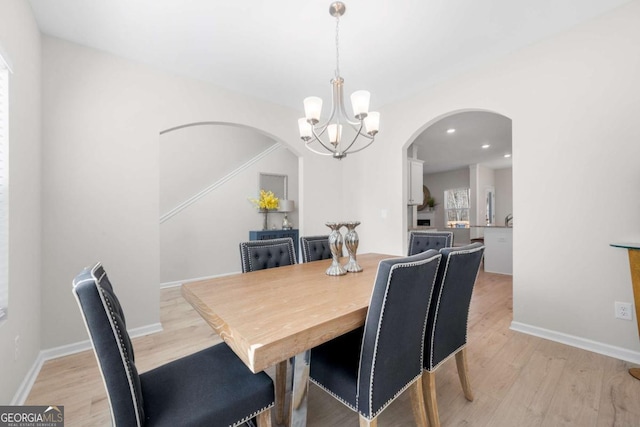 dining space featuring arched walkways, a notable chandelier, light wood-type flooring, and baseboards