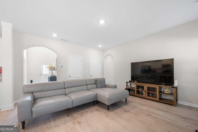 living area with visible vents, arched walkways, and light wood-style floors