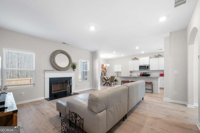 living room featuring recessed lighting, visible vents, light wood finished floors, and a fireplace with raised hearth