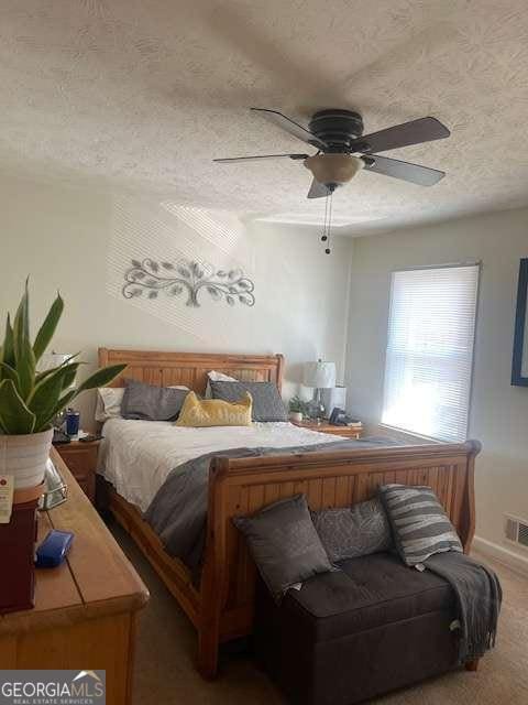 carpeted bedroom with ceiling fan, visible vents, and a textured ceiling