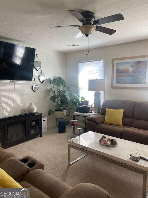 living room with light carpet, visible vents, a textured ceiling, and a ceiling fan