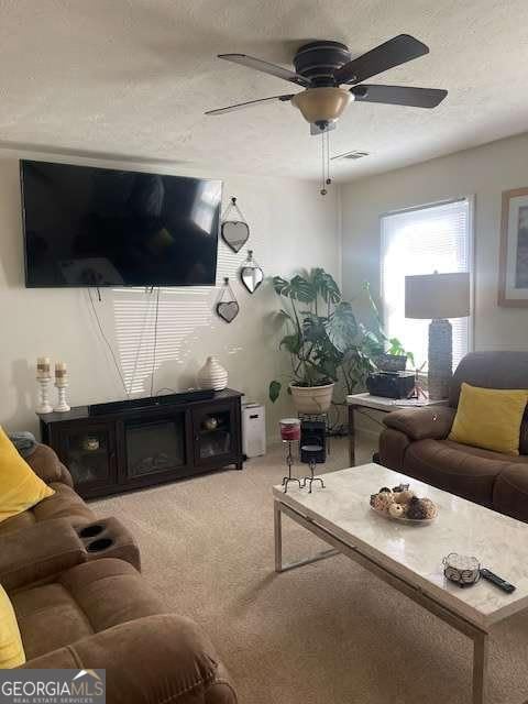 living room with a ceiling fan, light colored carpet, visible vents, and a textured ceiling