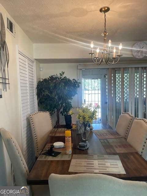 dining space with visible vents, a textured ceiling, and an inviting chandelier