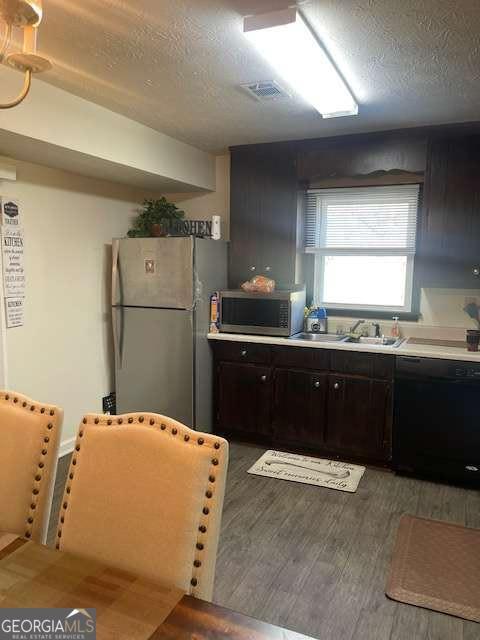 kitchen featuring stainless steel microwave, dishwasher, freestanding refrigerator, light wood-style floors, and a textured ceiling