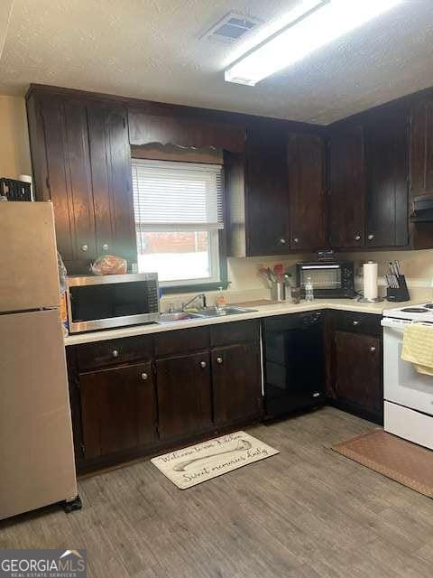 kitchen with dark brown cabinets, light countertops, light wood-type flooring, white appliances, and a textured ceiling