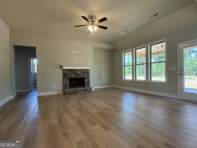 unfurnished living room featuring a stone fireplace, baseboards, visible vents, and wood finished floors