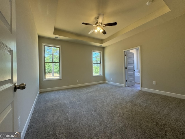 carpeted spare room featuring a tray ceiling, baseboards, visible vents, and ceiling fan