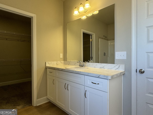 full bathroom with a walk in closet, wood finished floors, a shower, baseboards, and vanity