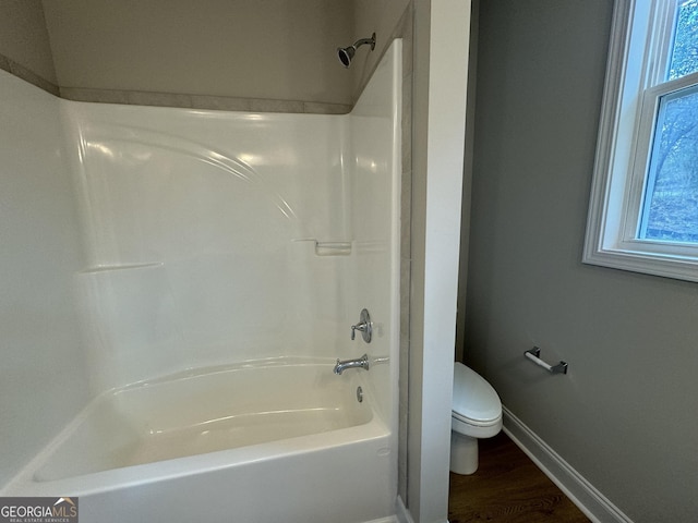 bathroom with shower / bathing tub combination, toilet, wood finished floors, and baseboards