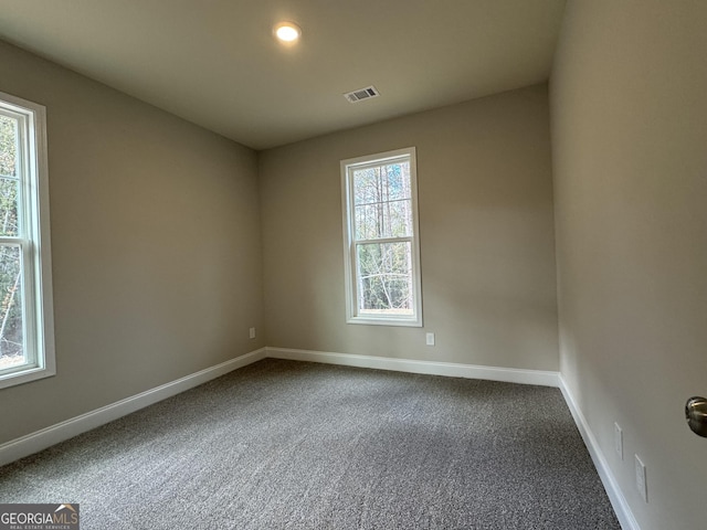 spare room with visible vents, plenty of natural light, dark carpet, and baseboards