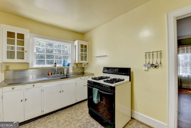 kitchen featuring a sink, stainless steel counters, baseboards, white cabinets, and gas range