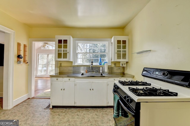 kitchen with a sink, stainless steel countertops, glass insert cabinets, white cabinetry, and white gas range