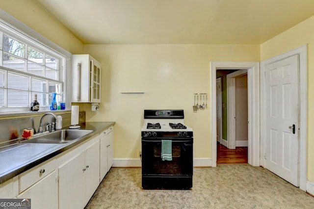 kitchen featuring light carpet, a sink, white cabinetry, range with gas cooktop, and baseboards