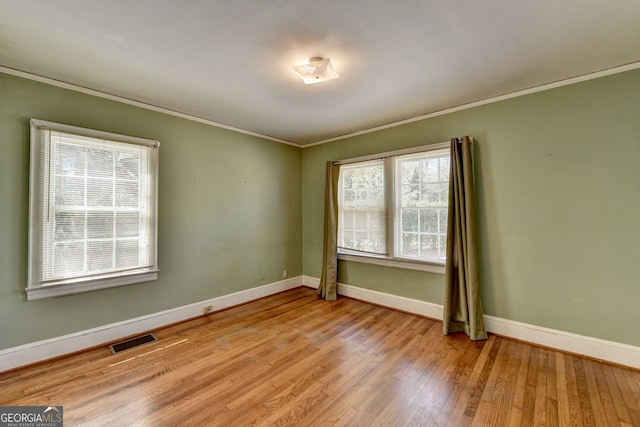 empty room featuring visible vents, crown molding, baseboards, and wood finished floors