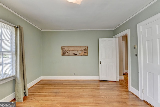 empty room featuring baseboards, crown molding, and light wood-style floors