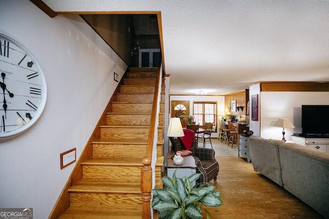 stairway featuring a textured ceiling, wood finished floors, and ornamental molding