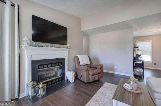 living room with a glass covered fireplace, baseboards, a textured ceiling, and wood finished floors