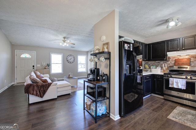 kitchen with gas stove, dark wood-type flooring, under cabinet range hood, backsplash, and black fridge