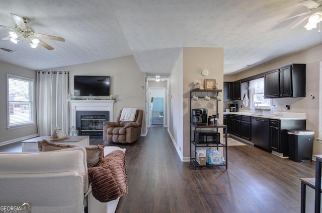 living room featuring a glass covered fireplace, visible vents, plenty of natural light, and dark wood-style floors