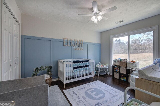 bedroom featuring visible vents, a crib, wood finished floors, a decorative wall, and a textured ceiling