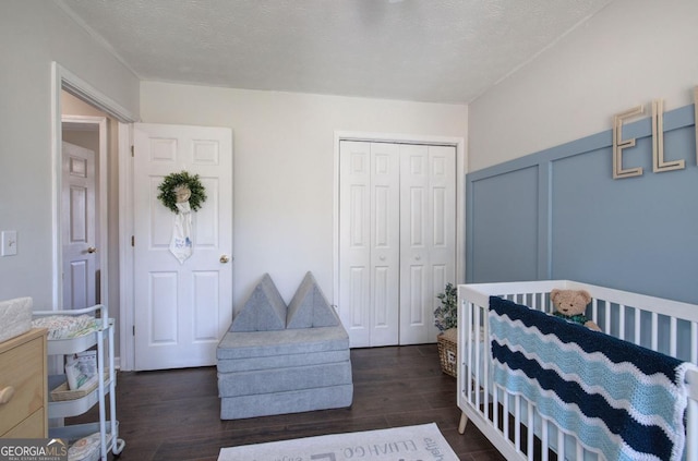 bedroom with a closet, a textured ceiling, dark wood-style floors, and a decorative wall